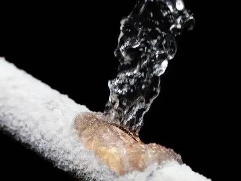 Frost-covered pipe split open and spraying water after a hard freeze
